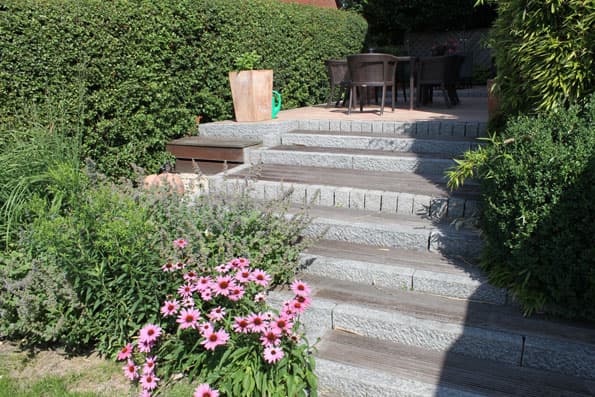 Natursteintreppe mit Blockstufen zwischen zwei Terrassenebenen im Garten