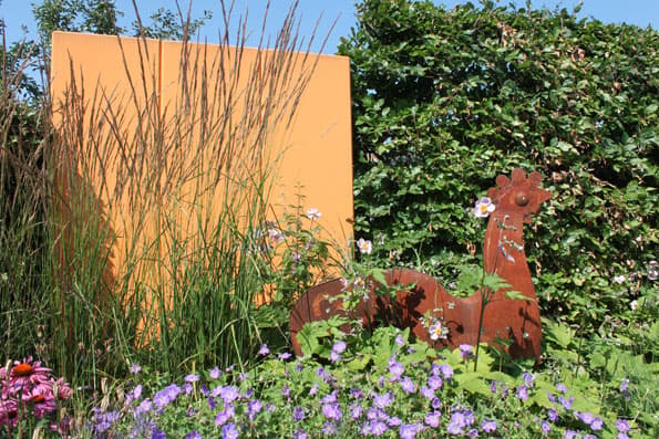 Staudenbeet mit Rost-Skulptur vor oranger Gestaltungswand
