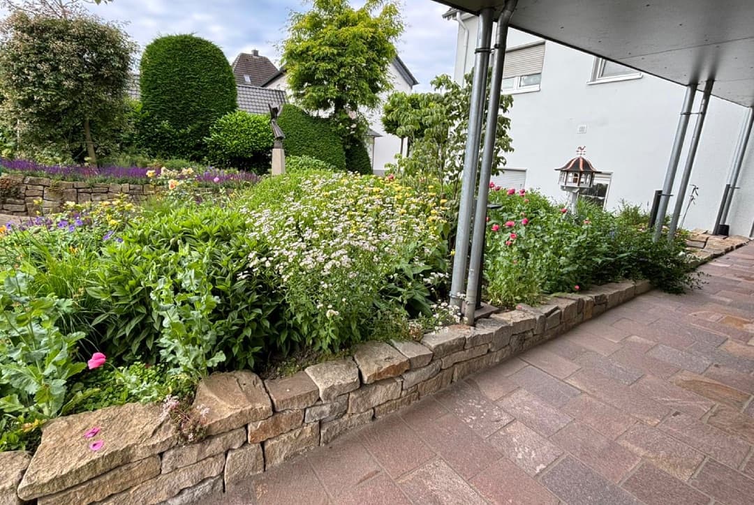 Natursteinmauer mit farbenfrohem Blumenbeet vor Terrasse